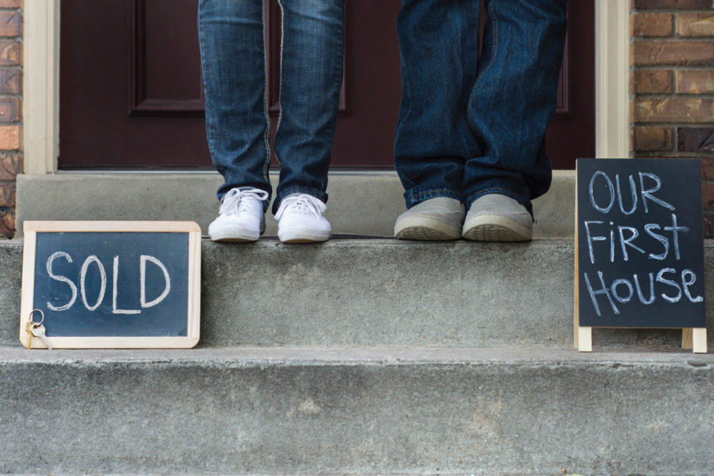 couple standing on step with sold and our first house