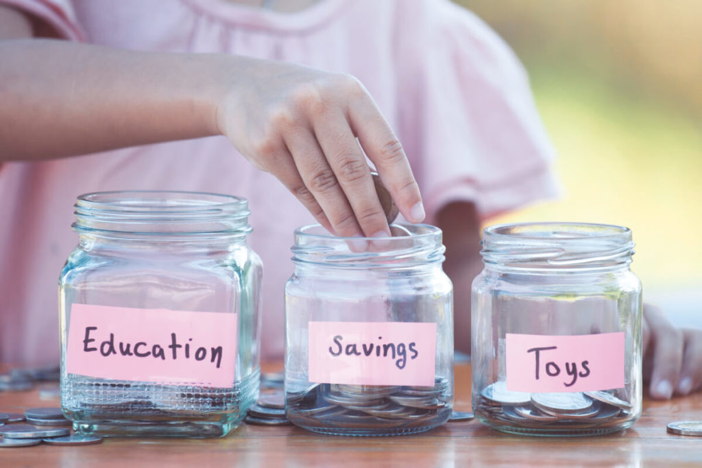Child putting savings money into three different jars called education, savings, and toys